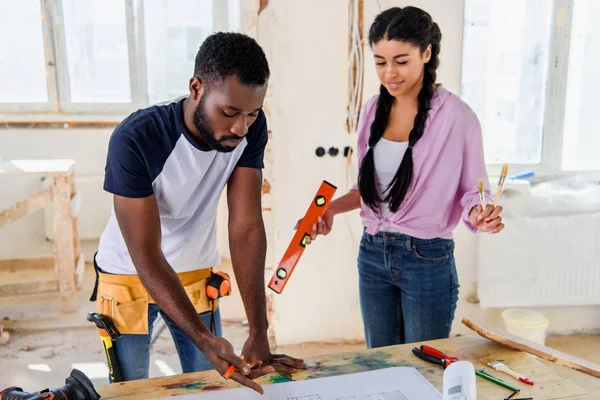 Beau jeune homme pointant vers le plan de la petite amie attrayante debout près pendant la rénovation de la maison — Photo de stock