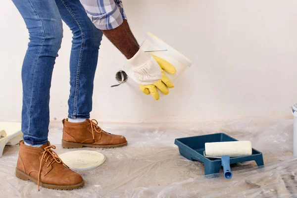 Imagen recortada del hombre en guantes de protección verter pintura en la bandeja de rodillos durante la renovación del hogar - foto de stock