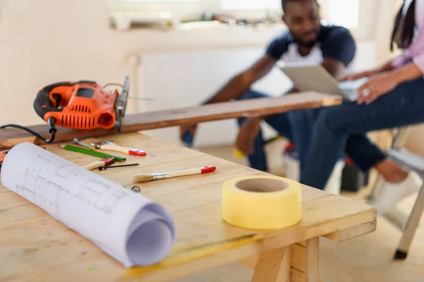 Selektiver Fokus von Holztisch mit Blaupause und zurücksitzendem Paar bei Renovierung zu Hause — Stockfoto