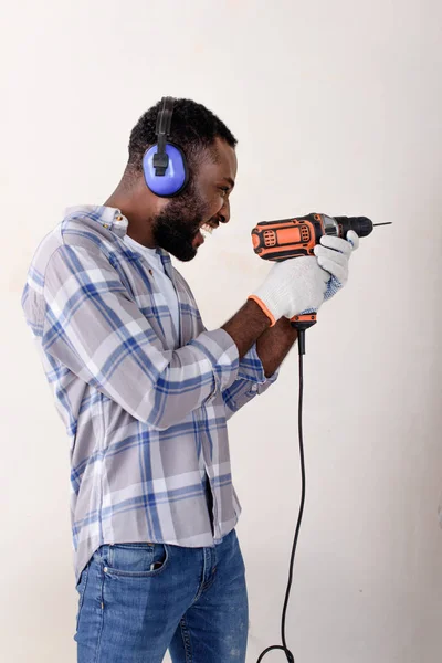 Happy young african american man in protective headphones and gloves having fun with power drill — Stock Photo