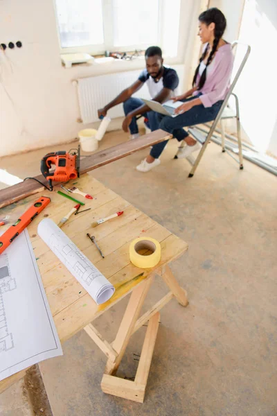 Vue grand angle de la table en bois avec plan et couple assis derrière pendant la rénovation à la maison — Photo de stock