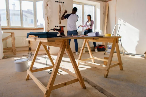 Foco seletivo de mesa de madeira com instrumentos e casal fazendo renovação atrás em casa — Fotografia de Stock