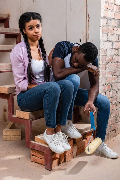 Jeune femme américaine afircan réconfortant petit ami fatigué avec rouleau de peinture pendant la rénovation de la maison — Photo de stock