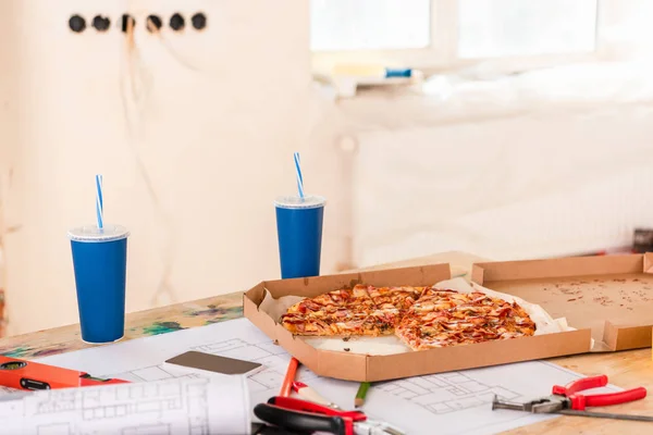 Foco seletivo de pizza, refrigerante, blueprint, ferramentas e smartphone com tela em branco na mesa — Fotografia de Stock