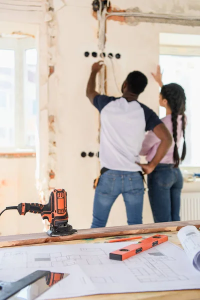 Selective focus of table with blueprint and couple making renovation behind at new home — Stock Photo