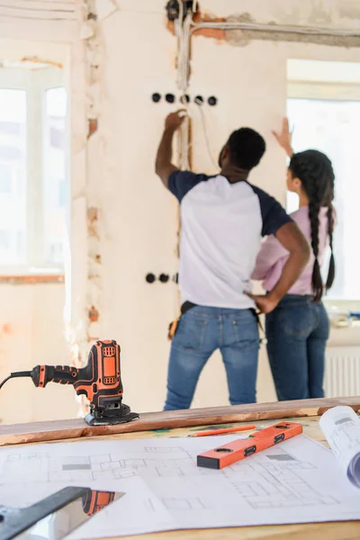 Foyer sélectif de la table avec le plan et le couple faisant la rénovation derrière à la nouvelle maison — Photo de stock