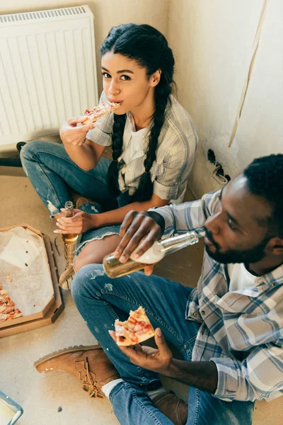 Vista ad alto angolo di coppia afro-americana mangiare pizza e bere birra durante la ristrutturazione a casa — Foto stock