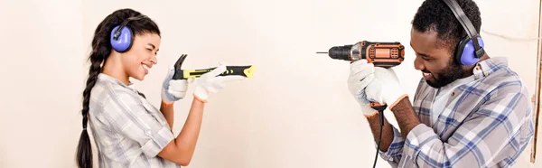 Side view of couple in protective headphones having fun with tools during renovation of home — Stock Photo