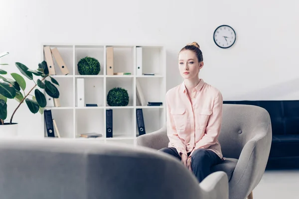 Attractive pensive businesswoman sitting in armchair in office and looking away — Stock Photo