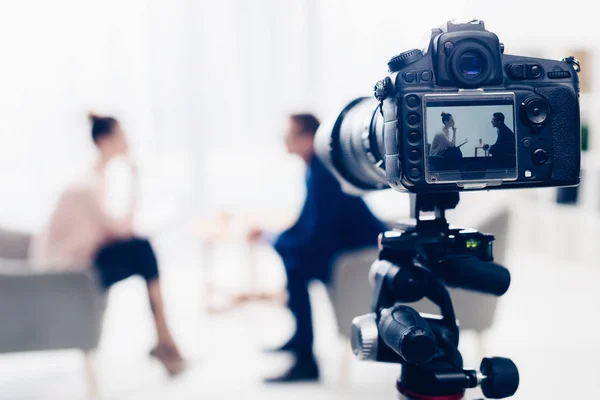 Empresário dando entrevista ao jornalista no escritório, câmera no tripé em primeiro plano — Fotografia de Stock