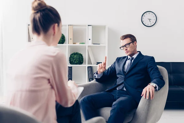 Hombre de negocios guapo mostrando un dedo hacia arriba mientras que da entrevista a periodista en la oficina - foto de stock