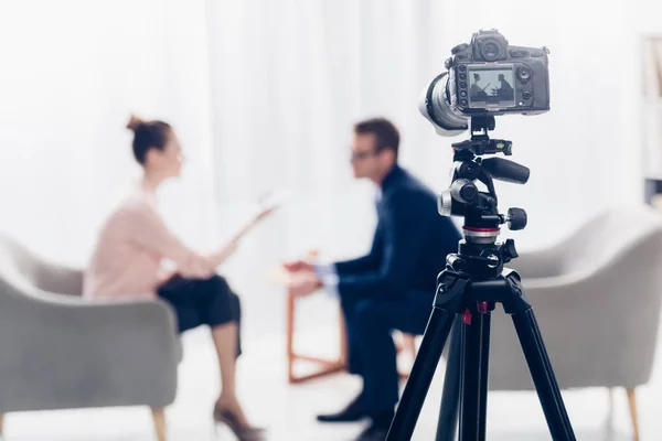 Empresário dando entrevista ao jornalista no escritório, câmera no tripé em primeiro plano — Fotografia de Stock