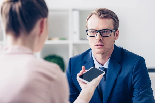 Guapo hombre de negocios en gafas y traje dando entrevista a periodista en la oficina - foto de stock