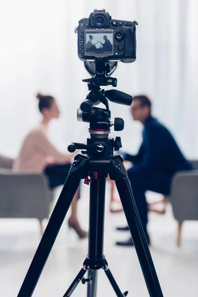 Side view of businessman giving interview to journalist in office, camera on tripod on foreground — Stock Photo