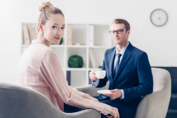 Schöner Geschäftsmann, der eine Tasse Tee hält, schöne Journalistin, die im Büro in die Kamera schaut — Stockfoto