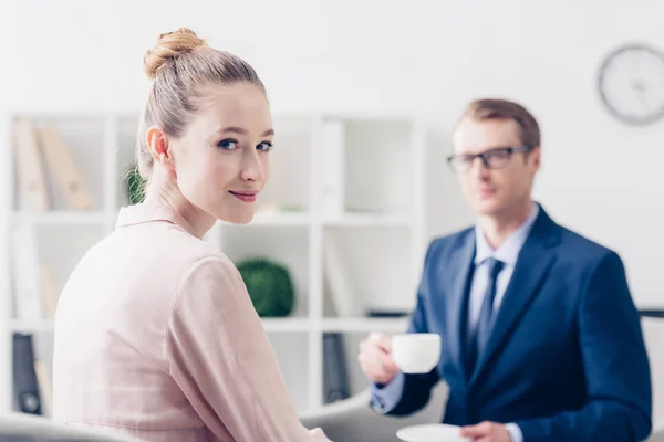 Handsome businessman holding cup of tea, attractive journalist looking at camera in office — Stock Photo