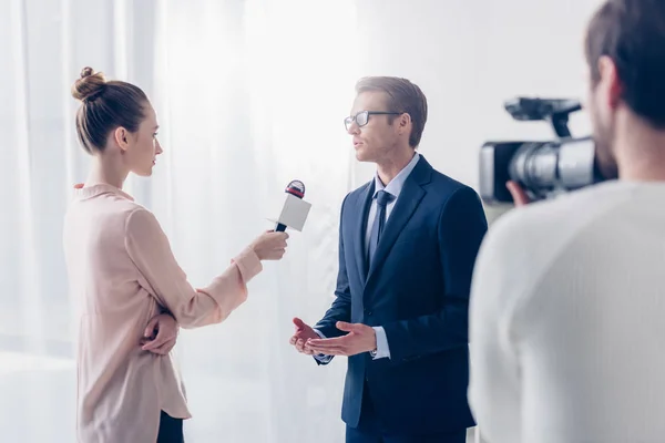 Guapo hombre de negocios en gafas dando video entrevista a hermosa periodista en la oficina - foto de stock