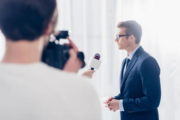 Foco seletivo de empresário bonito em óculos dando entrevista em vídeo para jornalista no escritório — Fotografia de Stock