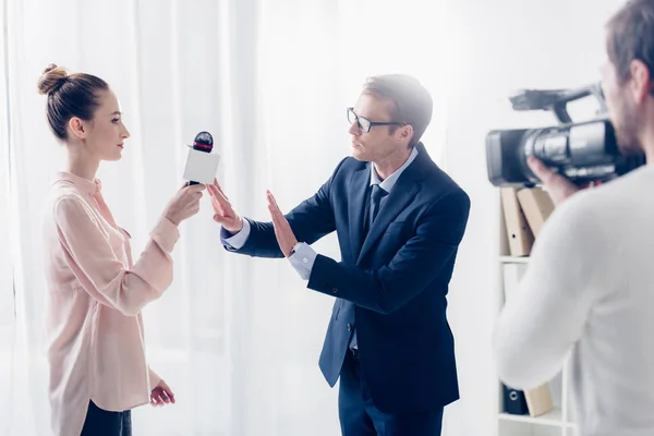 Bel homme d'affaires en costume refusant de donner une interview vidéo au journaliste et ne montrant aucun geste au bureau — Photo de stock