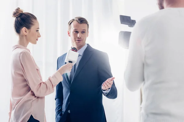 Gut aussehender Geschäftsmann gibt Journalisten ein Videointerview und gestikuliert im Büro — Stockfoto