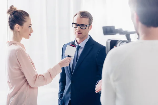 Handsome businessman in glasses giving video interview to journalist in office — Stock Photo