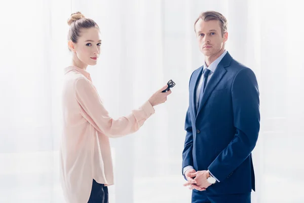 Schöner Geschäftsmann gibt attraktiven Journalisten mit Diktiergerät im Büro ein Interview und schaut in die Kamera — Stockfoto