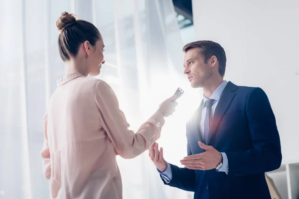 Vue en angle bas d'un bel homme d'affaires donnant une interview à un journaliste avec enregistreur de voix au bureau — Photo de stock