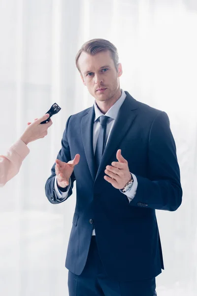 Abgeschnittenes Bild eines gutaussehenden Geschäftsmannes, der einem Journalisten mit Diktiergerät ein Interview gibt und im Büro in die Kamera schaut — Stockfoto