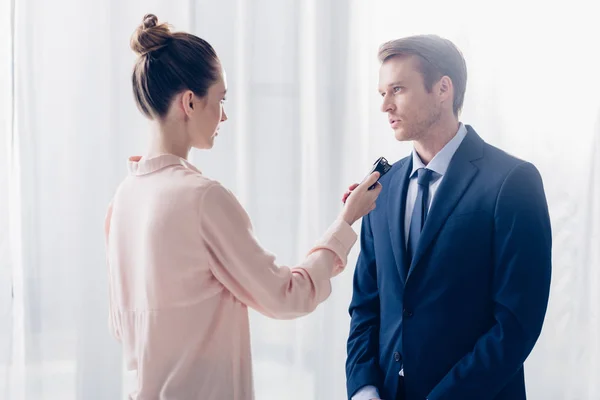 Side view of handsome businessman giving interview to journalist with voice recorder in office — Stock Photo