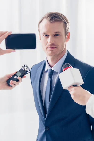 Bonito empresário dando entrevista para jornalistas e olhando para câmera no escritório — Fotografia de Stock