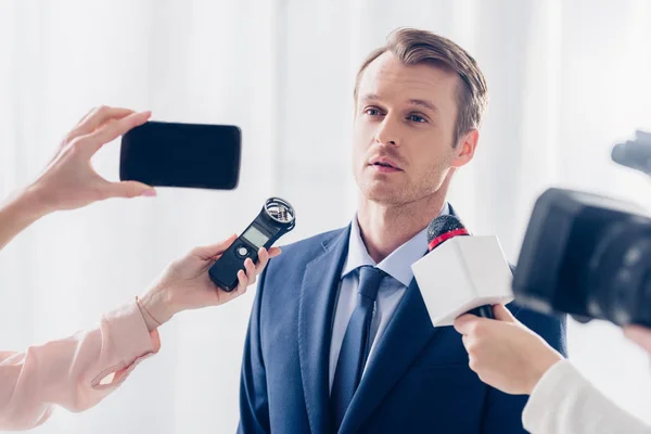 Bonito empresário dando entrevista para jornalistas e olhando para longe no escritório — Fotografia de Stock