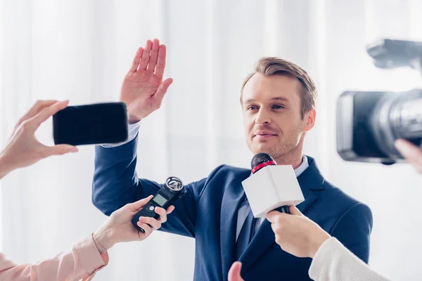 Apuesto hombre de negocios dando entrevista a periodistas en el cargo y saludando la mano - foto de stock