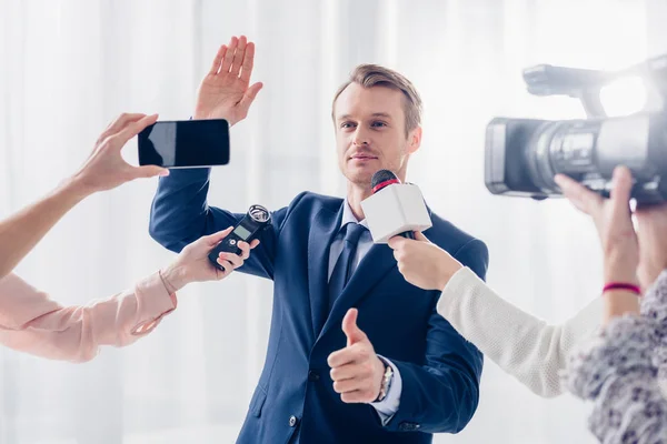 Schöner Geschäftsmann gibt Journalisten im Amt ein Interview, winkt mit der Hand und zeigt den Daumen nach oben — Stock Photo