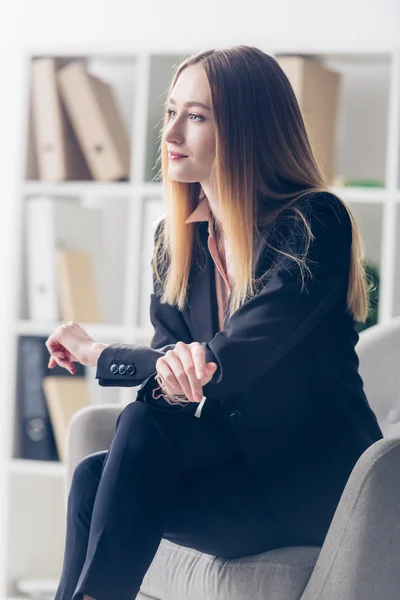 Vue latérale de la femme d'affaires attrayante en costume assis sur un fauteuil et regardant loin dans le bureau — Photo de stock