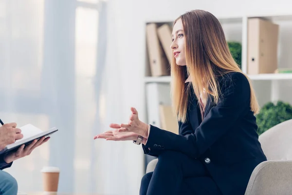 Cropped image of businesswoman in suit giving interview to journalist and gesturing in office — Stock Photo