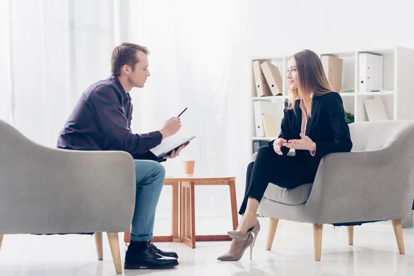 Side view of beautiful businesswoman in suit giving interview to journalist in office — Stock Photo