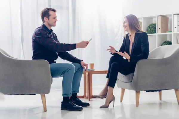 Side view of happy businesswoman in suit giving interview to journalist in office — Stock Photo