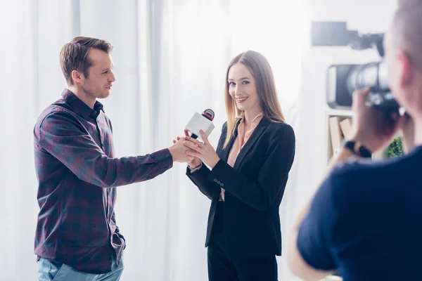 Beautiful businesswoman in suit giving interview to journalist, holding microphone and looking at camera in office — Stock Photo