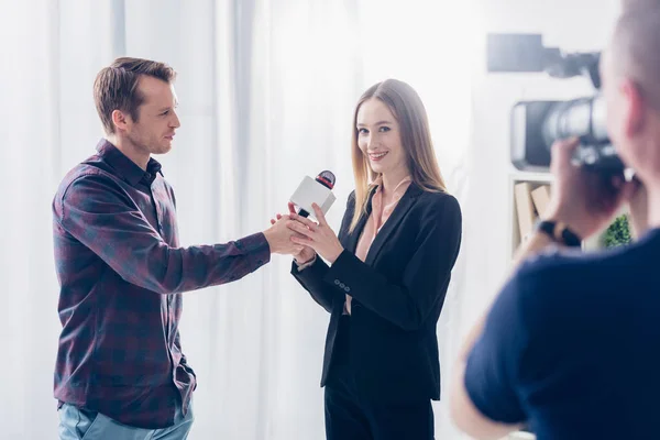 Hermosa mujer de negocios en traje dando entrevista a periodista, sosteniendo el micrófono y mirando a la cámara en la oficina - foto de stock