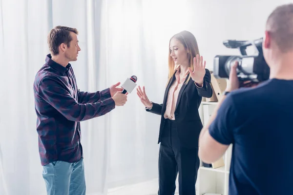 Beautiful businesswoman in suit rejecting giving interview to journalist and showing stop sing to cameraman in office — Stock Photo