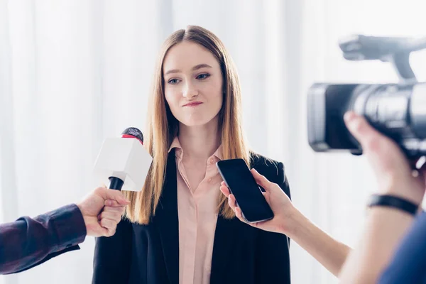 Grimacing businesswoman giving interview to journalists in office — Stock Photo