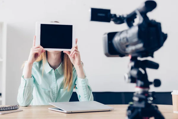 Жінка-відео блогер записує відеоблог і покриває обличчя планшетом з порожнім екраном в офісі — стокове фото