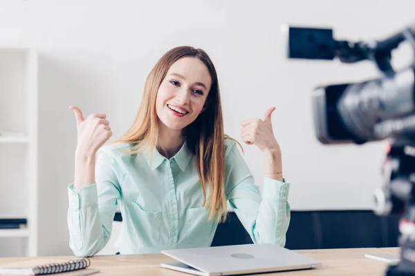 Sorrindo atraente fêmea vídeo blogger gravação vlog e mostrando polegares para cima no escritório — Fotografia de Stock