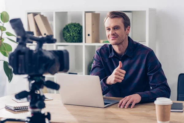 Sorrindo bonito macho vídeo blogger gravação vlog e mostrando polegar no escritório — Fotografia de Stock