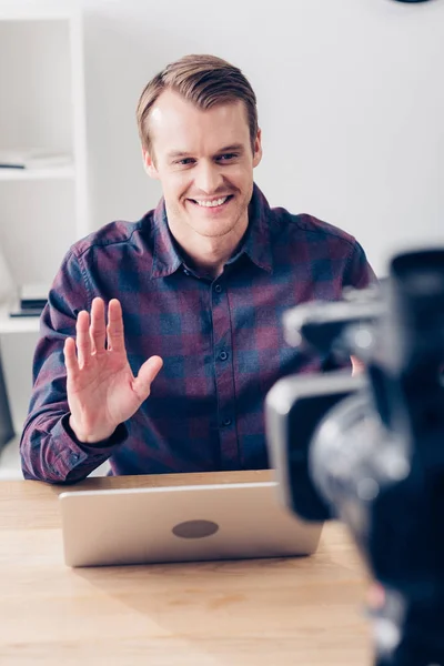 Lächelnd gut aussehender männlicher Videoblogger, der Vlog aufzeichnet und im Büro mit der Hand winkt — Stockfoto