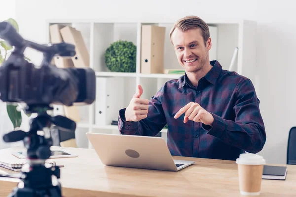 Souriant beau mâle vidéo blogueur enregistrement vlog et montrant pouce au bureau — Photo de stock