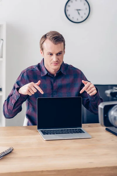 Handsome male video blogger recording vlog and pointing on laptop with blank screen in office — Stock Photo