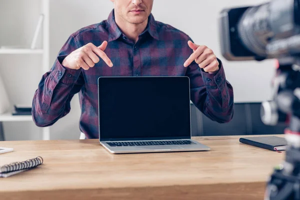 Cropped image of male video blogger recording vlog and pointing on laptop with blank screen in office — Stock Photo