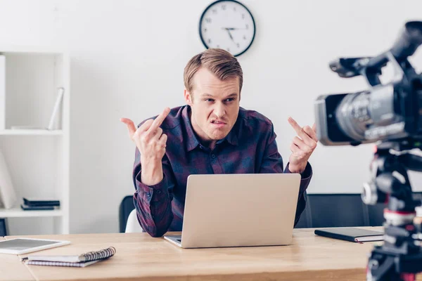 Aggressive male video blogger recording vlog and showing middle fingers in office — Stock Photo