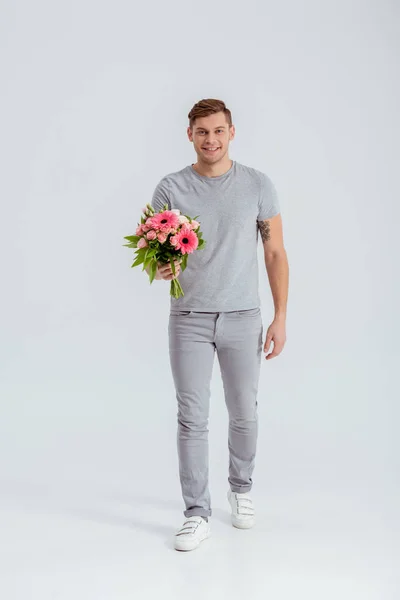 Homme regardant caméra et tenant bouquet de fleurs rose isolé sur gris — Photo de stock